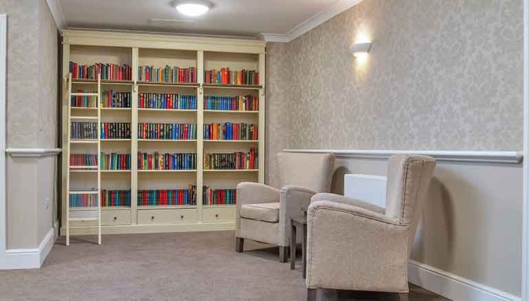 A cosy library with two beige armchairs facing a built-in bookshelf filled with colourful books