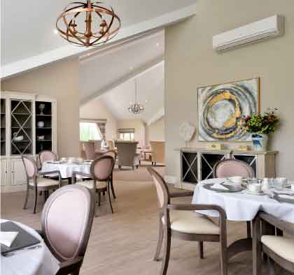 Beautifully laid up dining room with multiple tables set for a meal, pink upholstered chairs, a chandelier, and artwork on the walls. 