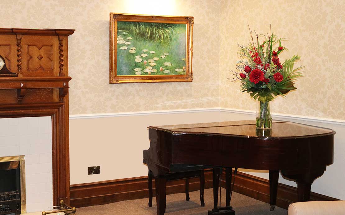 A grand piano with a large floral arrangement on top, in a room with a painting of water lilies above it