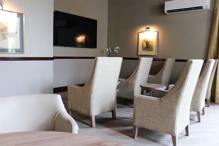 A lounge and theatre room with cream  upholstered chairs, a  wooden table, and wall-mounted television