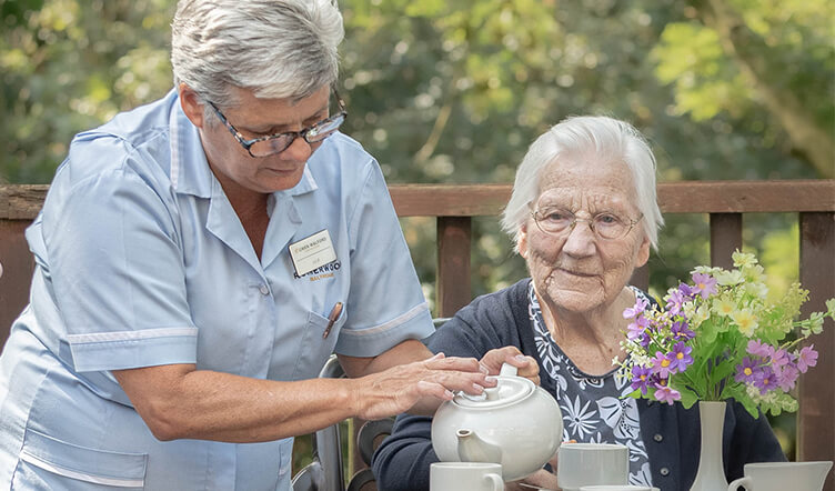 Healthcare worker pours an elderly lady a cup of tea outside