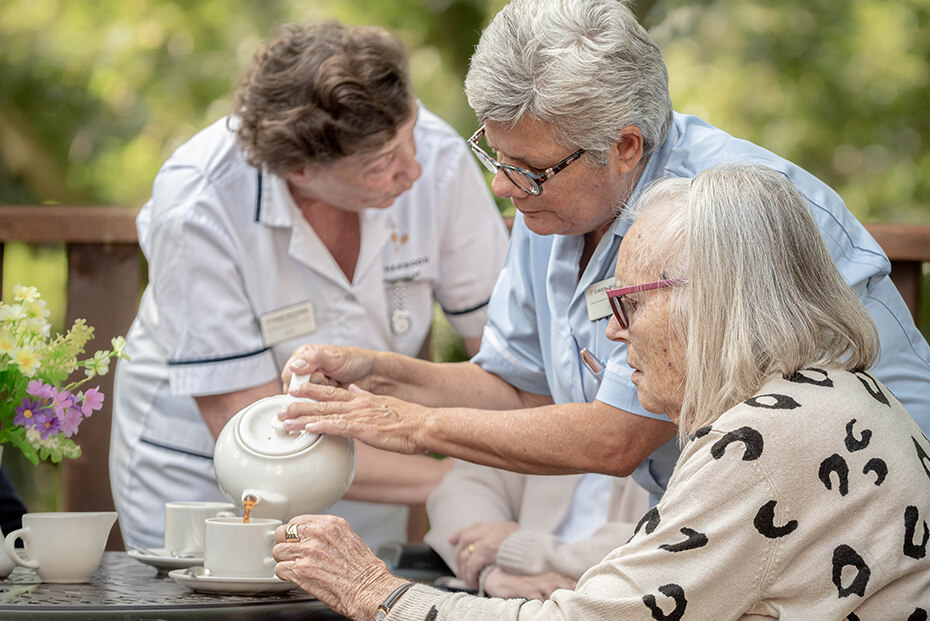 Healthcare worker pours an older lady  a cup of tea outside