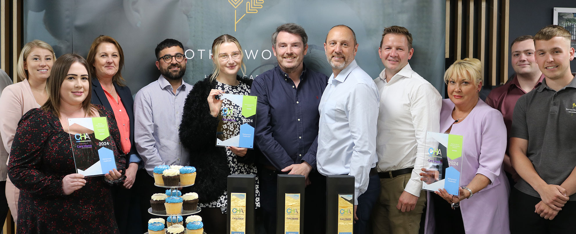 A group photo of staff celebrating an award win, with cakes and balloons