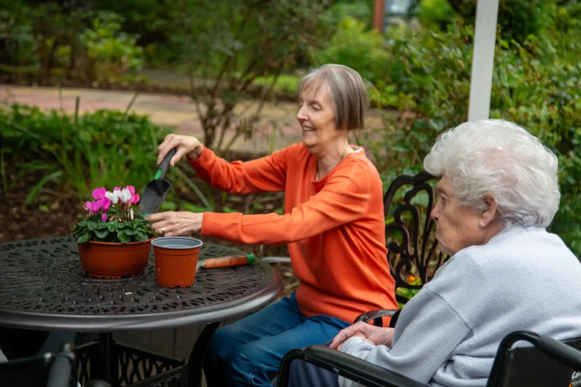 Two residents potting flowers at a table in the Dorset House garden