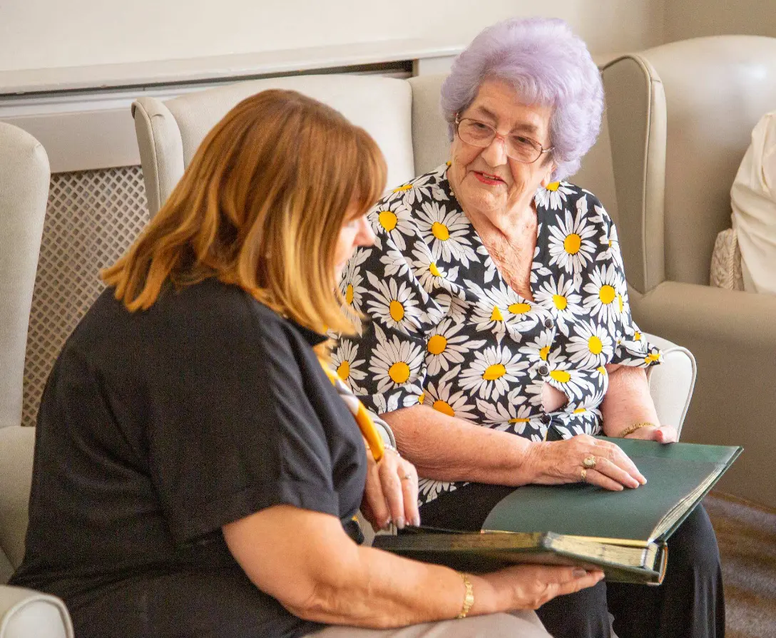 A member of the Dorset House team looking through a photo album with a resident in the lounge