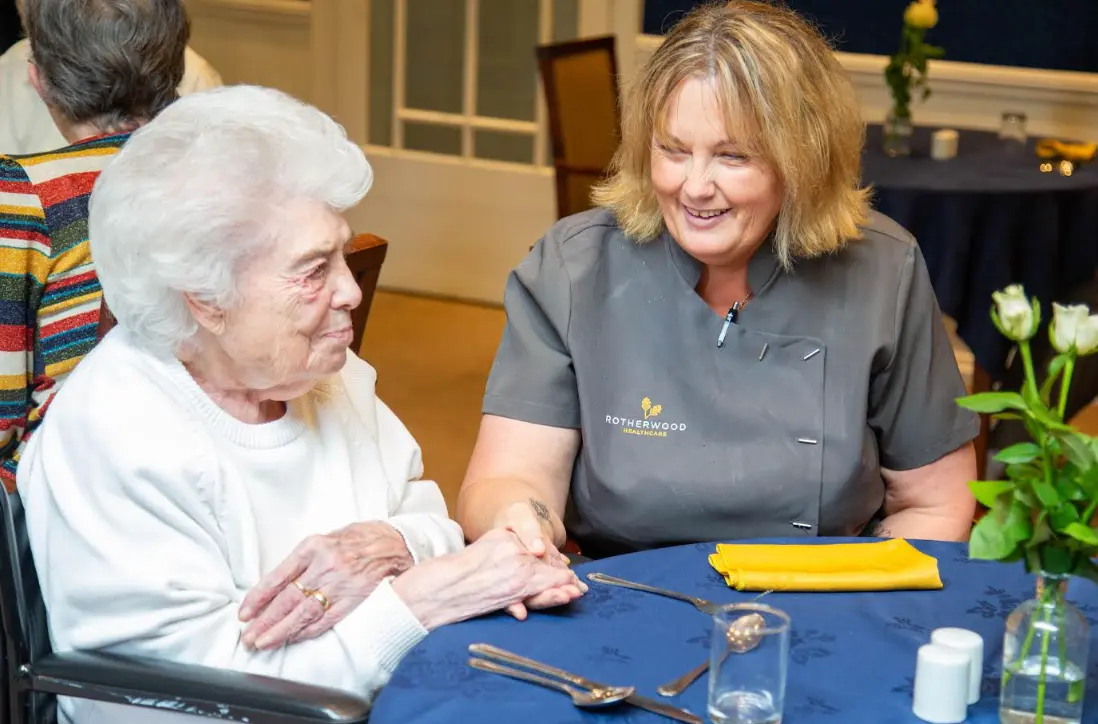 A member of the Dorset House team holding hands with a resident at a dining table