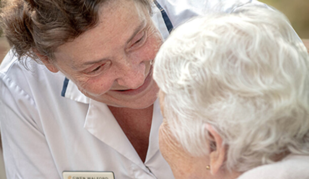 Close-up of a healthcare worker talking with and smiling at an elderly female resident