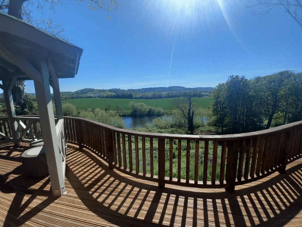 A wooden bench on a deck, surrounded by trees, overlooking a river