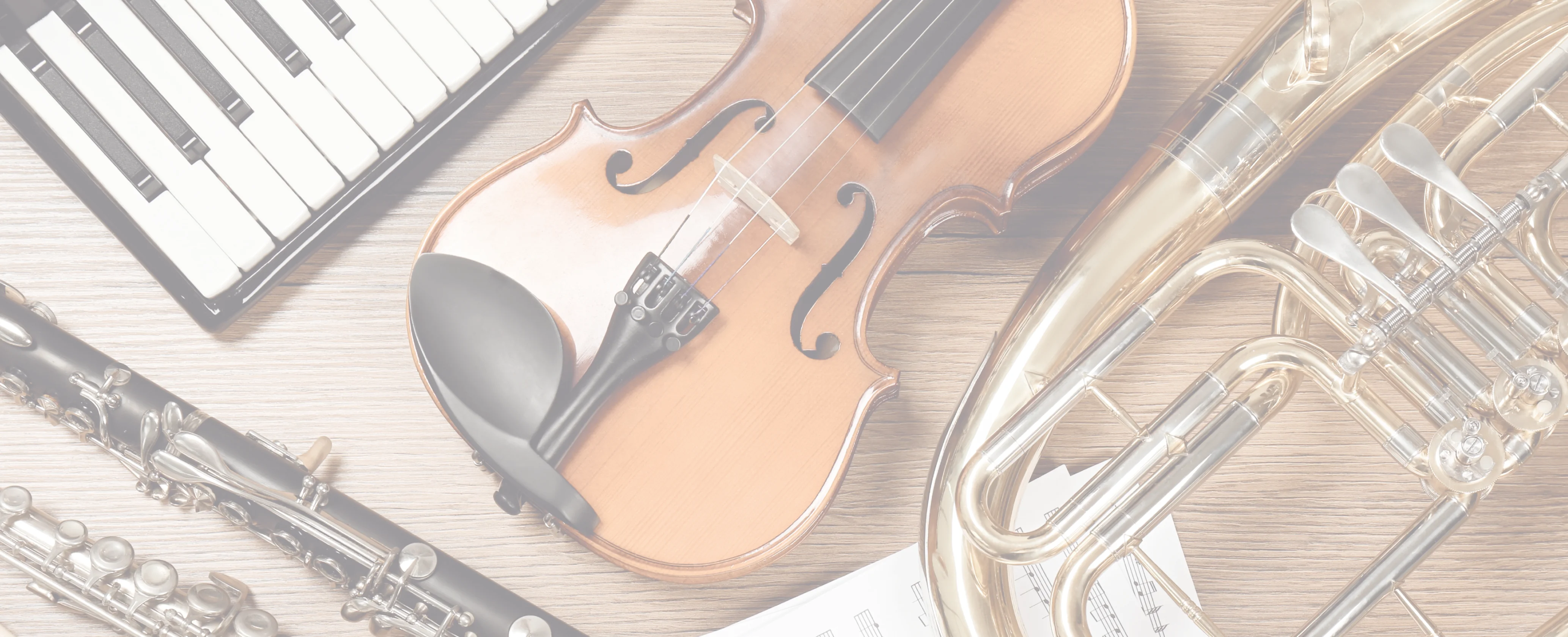 A keyboard, violin, clarinet, flute and brass instruments laid out on a pale wooden table