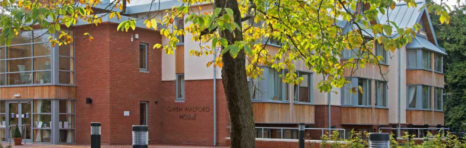 Modern brick building with large windows, located in a landscaped area with green trees.