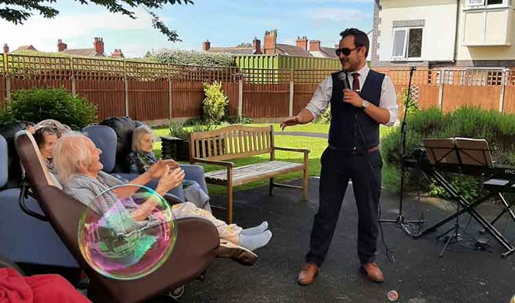 Formally dressed male singer performing outdoors, sings to an elderly lady seated in a chair 