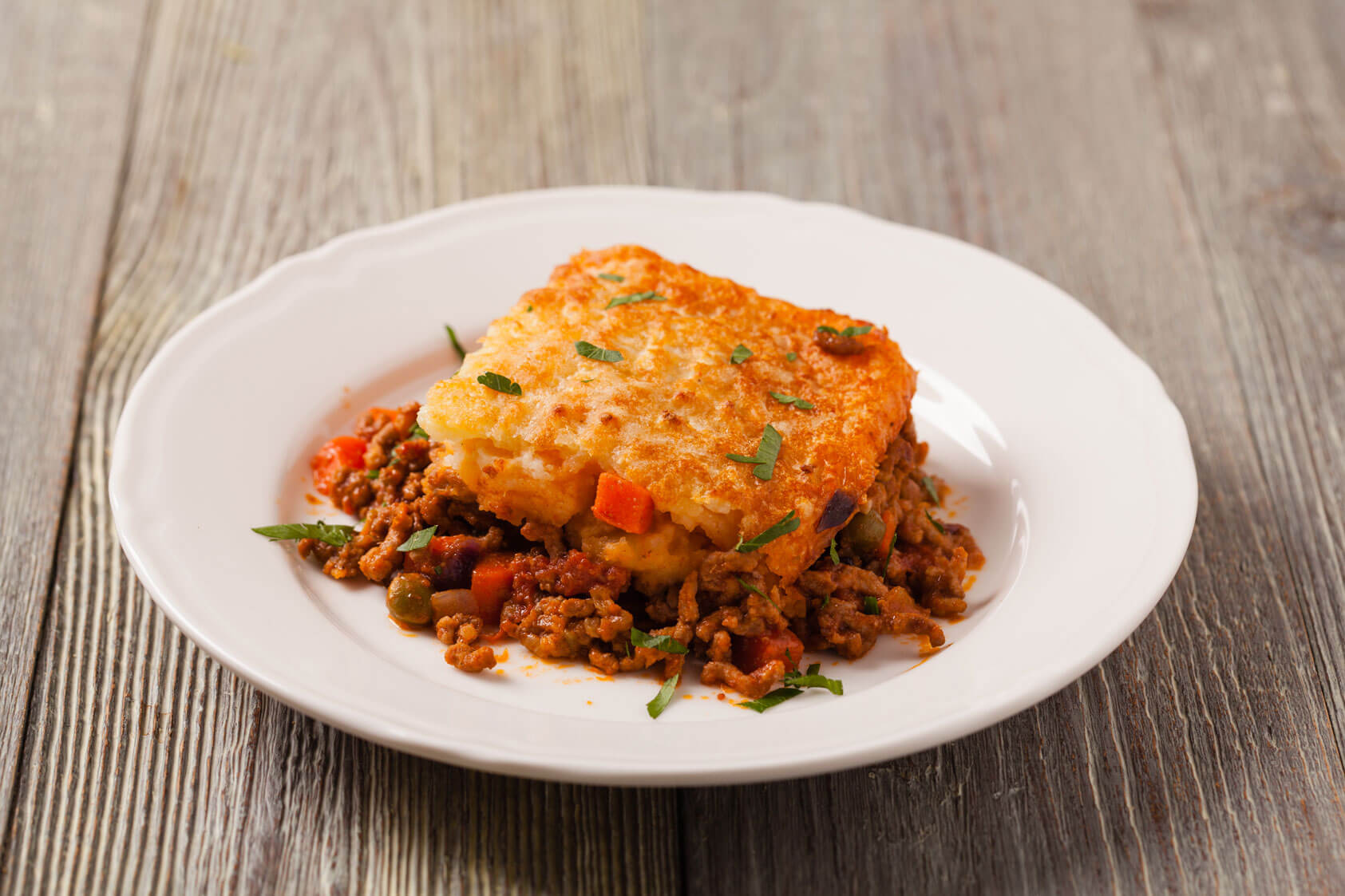 A slice of shepherd’s pie garnished with herbs, served on a white plate