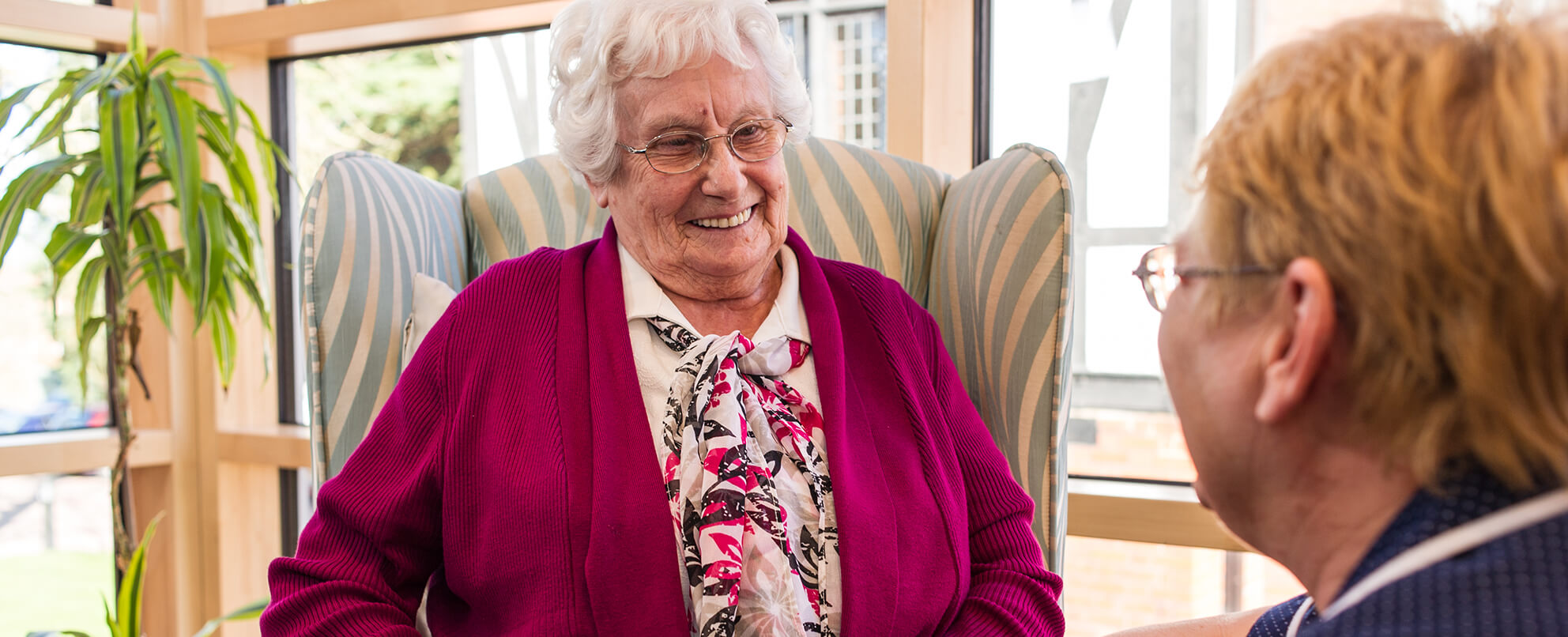 Elderly lady sits in chair and smiles at healthcare worker